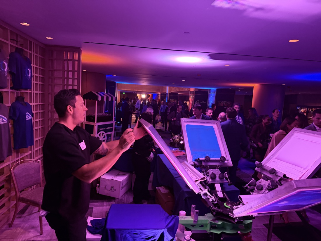 Merch Troop attendant working the press as an evening celebration fills the room behind him
